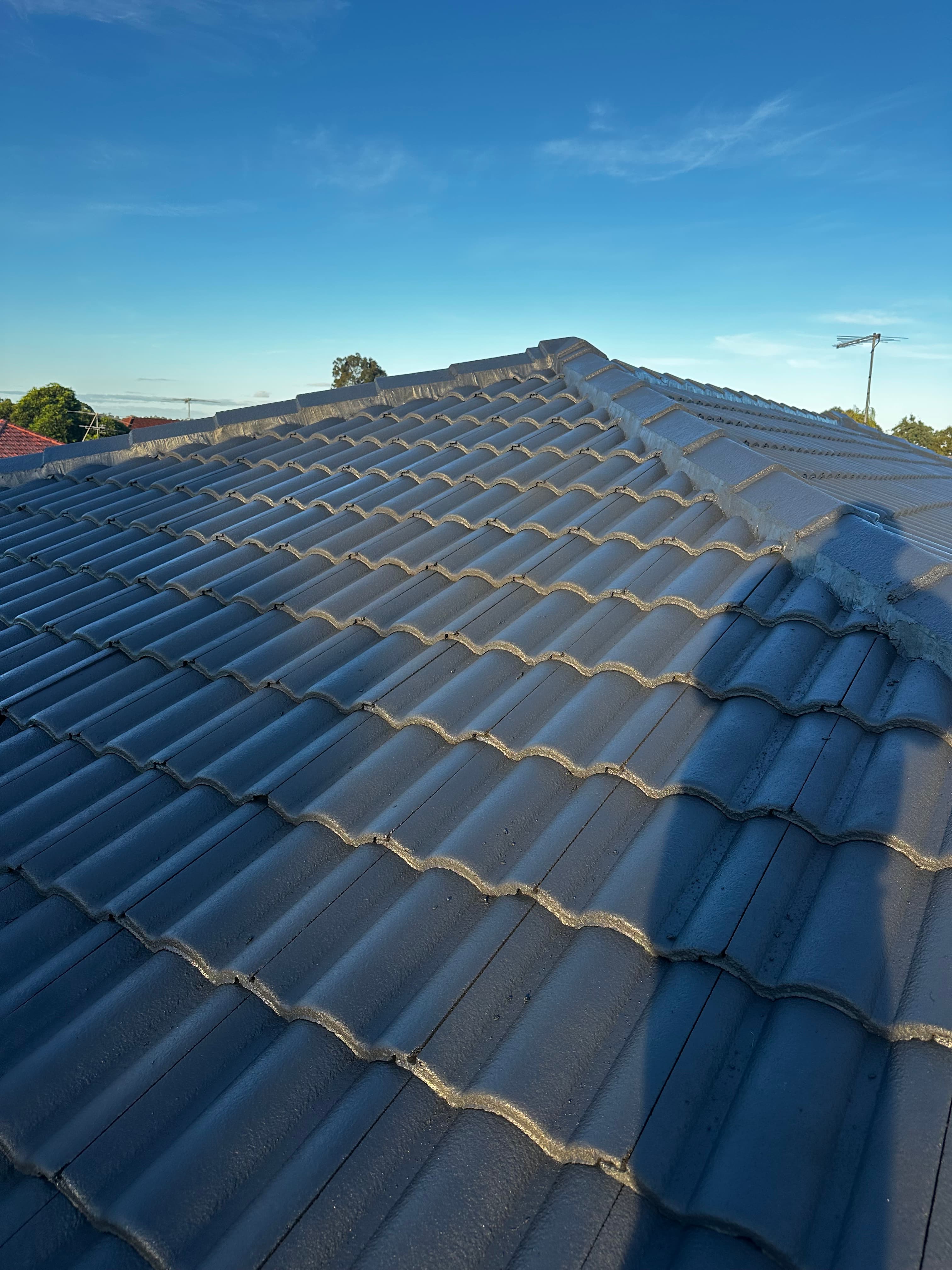 Dark grey concrete roof tiles with a wavy profile under a clear, bright blue sky.