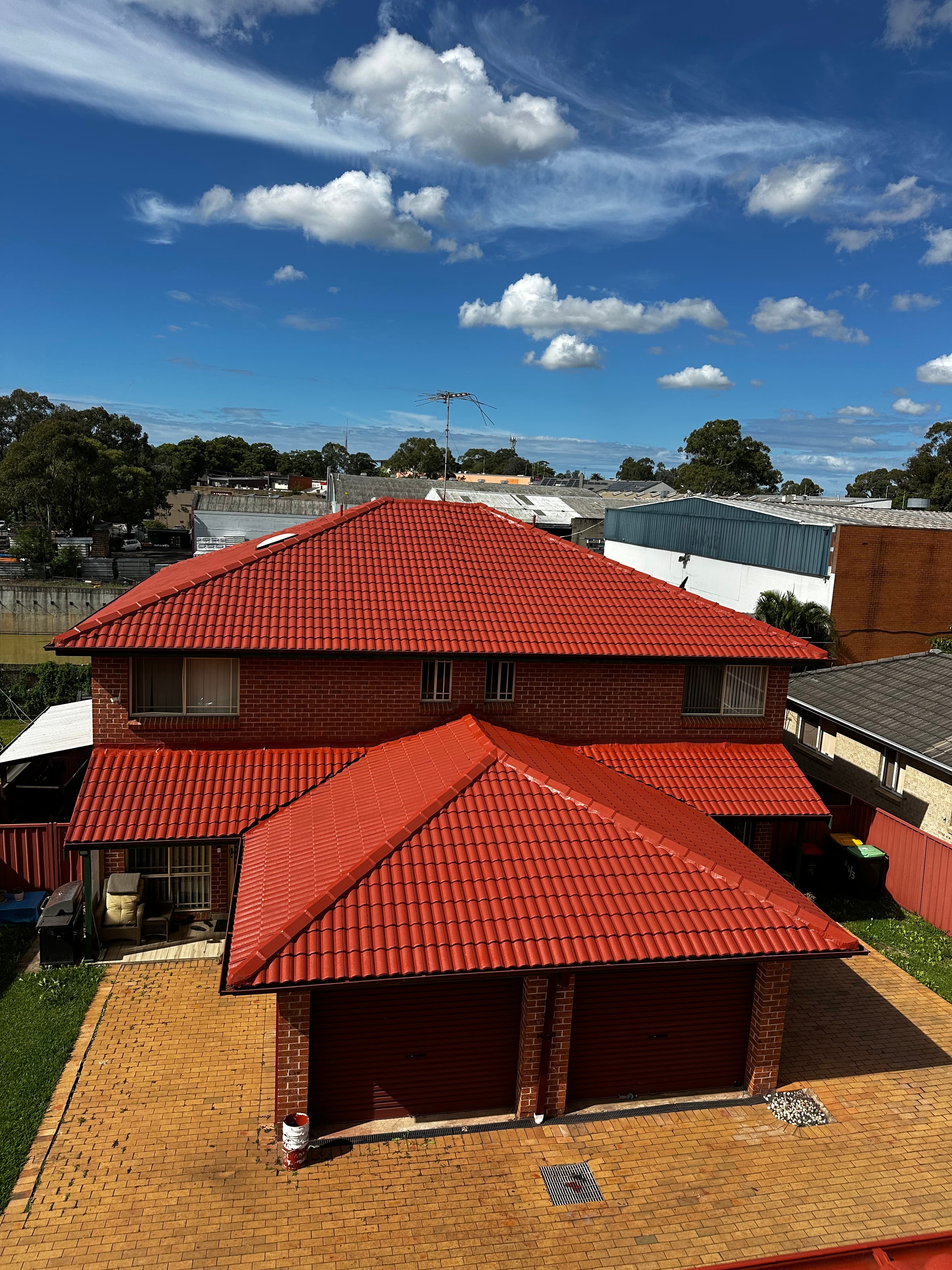Two-story red brick house with vibrant red tiled roof and double garage under blue sky.